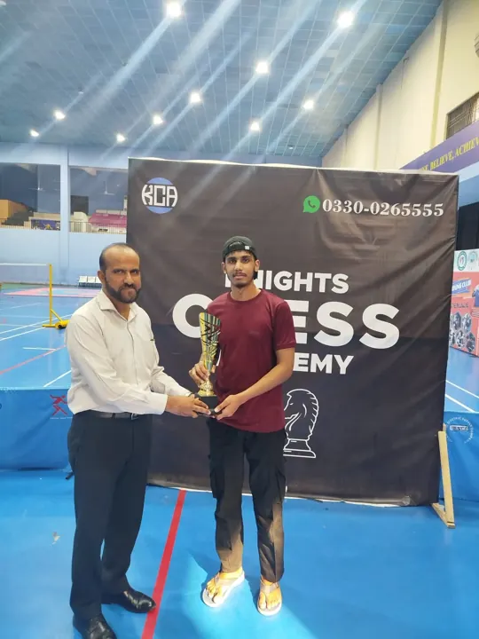 A young player in a maroon T-shirt receives a gold trophy from an organiser