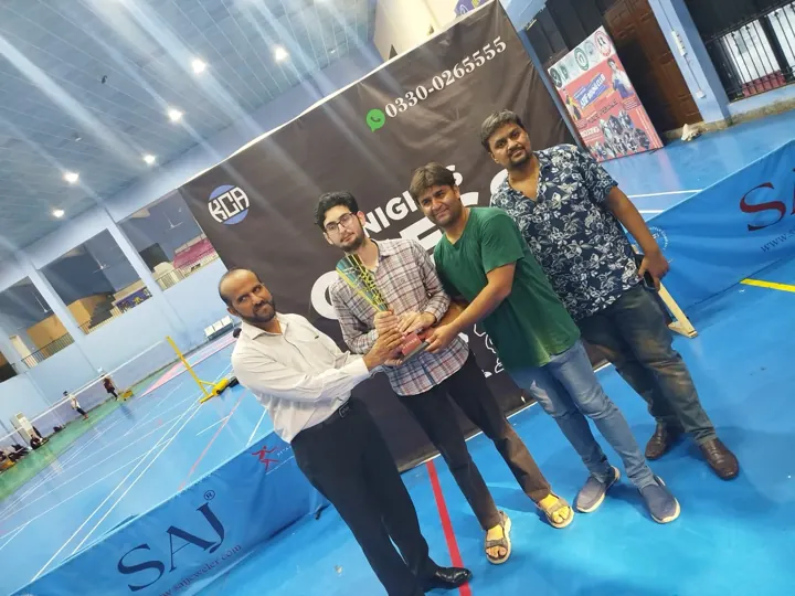 The tournament winner holds a gold trophy marked Winner, flanked by three organisers