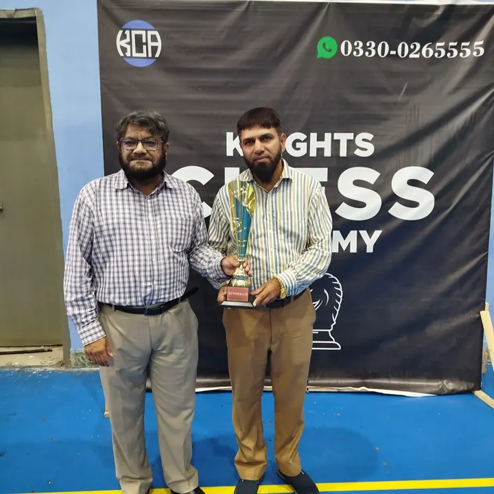 The runner-up, in a striped shirt, holds a gold trophy marked Runner-up beside an organiser