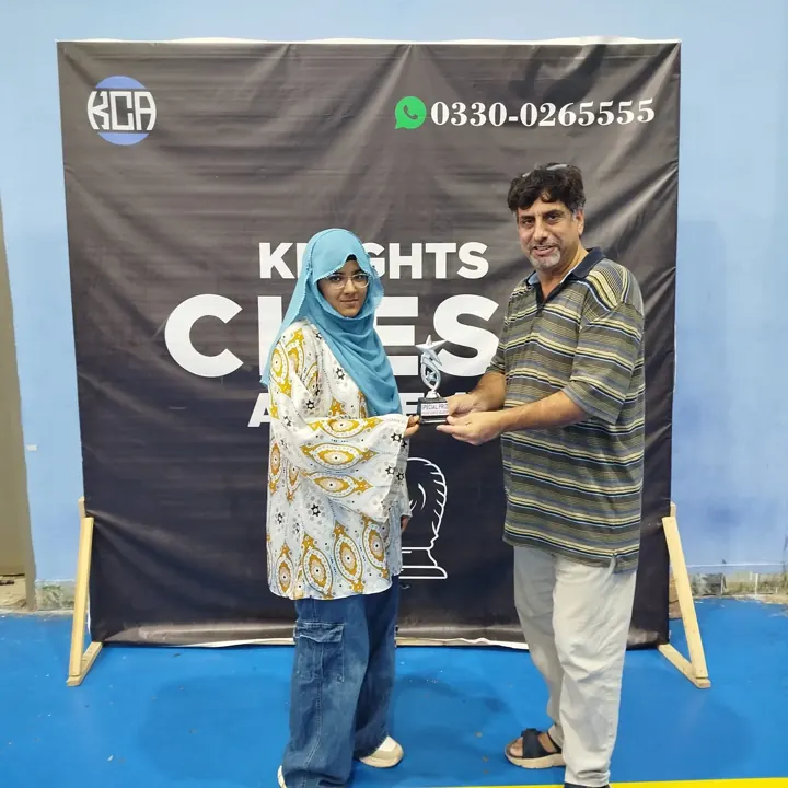 A girl in a blue hijab receives a star-topped special-prize trophy from an organiser