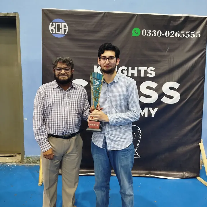 The winner, in a blue checked shirt, holds a tall gold trophy marked Winner beside an organiser